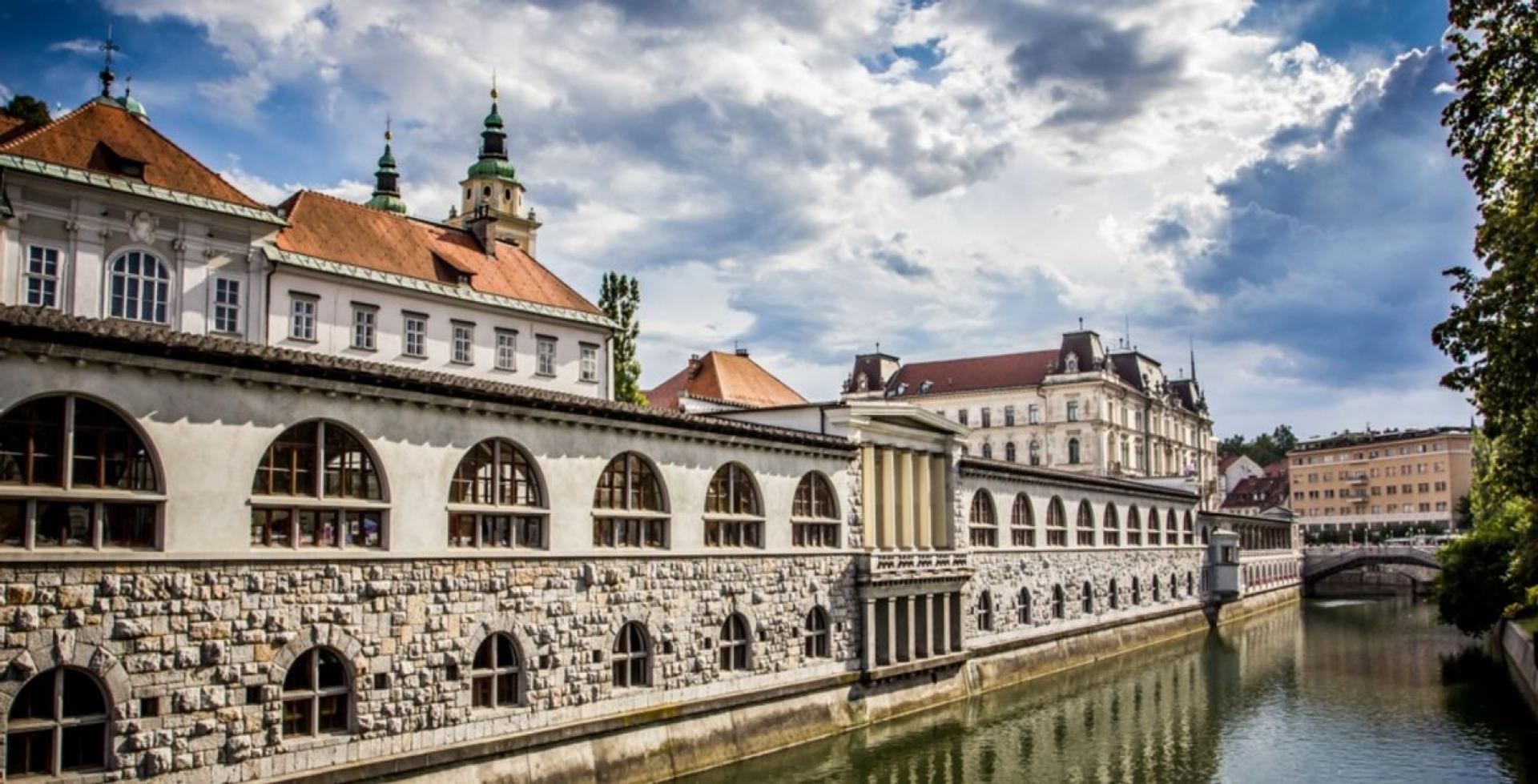 The market building by Joe Plečnik stretches between the Triple Bridge and the Dragon Bridge, on the right side of the curve of the Ljubljanica River.