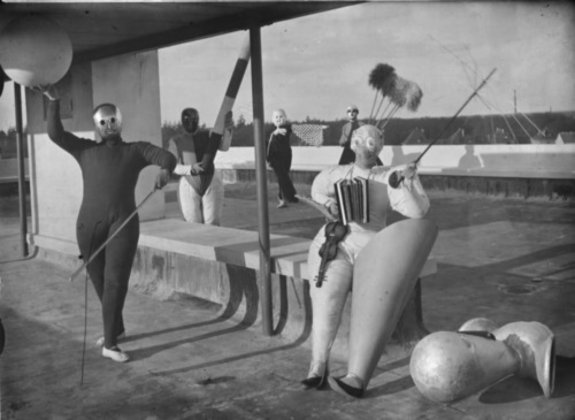 Pantomime “Treppenwitz”, members of the Bauhaus Stage in costumes on the roof of the workshop building, Hermann Röseler (with big stick and mask), Oskar Schlemmer, Roman Clemens (with requisite »A«) and Andor Weininger (as musical clown), 1927 | Photo © Erich Consemüller, Stiftung Bauhaus Dessau